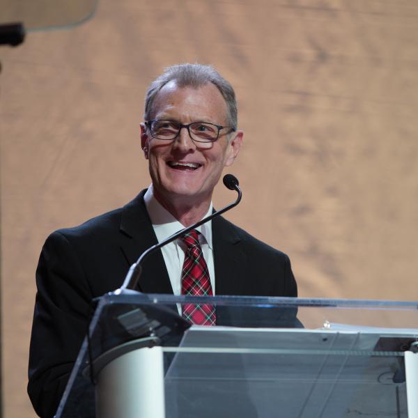 A man standing at a podium and smiling while on stage at the State Annual Meeting