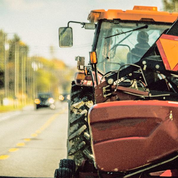Rear view of a tractor driving on a country road with a slow-moving vehicle indicator on it.