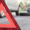 Close up of a slow moving vehicle sign placed in front of a car that is having its tire changed by a person