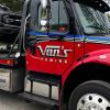 A flatbed tow truck with "VAN'S TOWING" painted on the side hauling an SUV down the road.